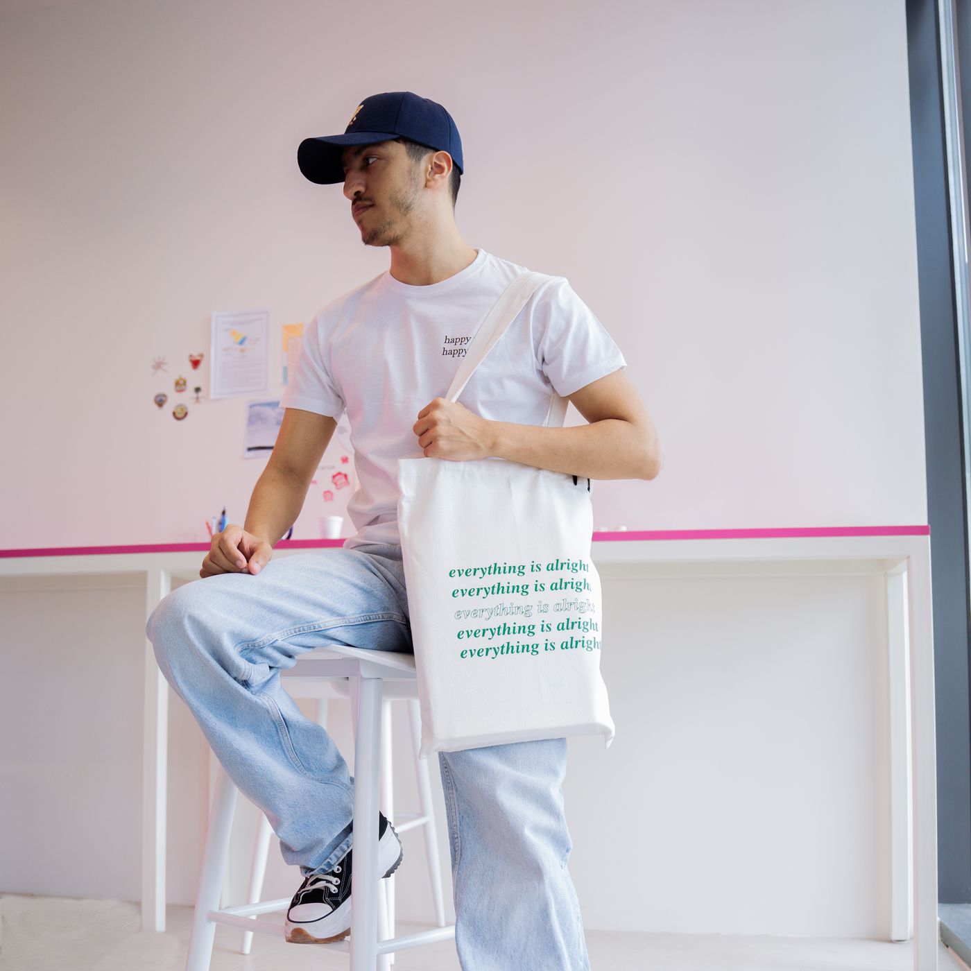 A student at the INK. studio wearing a custom cap and tee, holding a printed tote